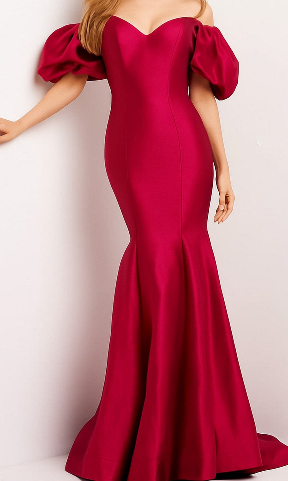 A person wearing the Jovani Puff-Sleeve Long Mermaid Prom Dress 09031 in red, featuring fitted, floor-length styling and off-the-shoulder puff sleeves, standing against a plain light background.